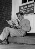 Publicity photograph taken during the Second World War of a soldier sitting on the step of Fort Slocum's library, then located in Building 69, reading a movie fan magazine.